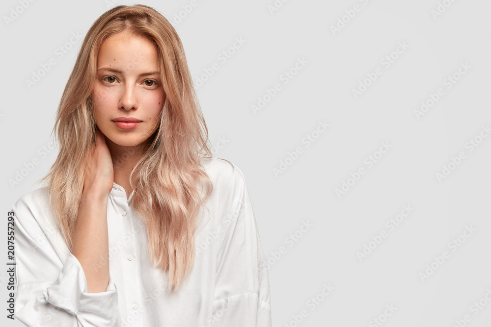 Studio shot of pretty light haired beautiful woman has luxurious hair, wears white casual oversized clothes, looks self assured and with calm expression at camera, isolated on white background Studio shot of pretty light haired beautiful woman has luxurious hair, wears white casual oversized clothes, looks self assured and with calm expression at camera, isolated on white background