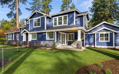 Beautiful luxury home exterior on sunny day with green grass, blue sky, and backdrop of trees