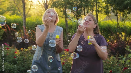 Two elderly women blowing bubbles. Elderly female friends having fun in the park together photo