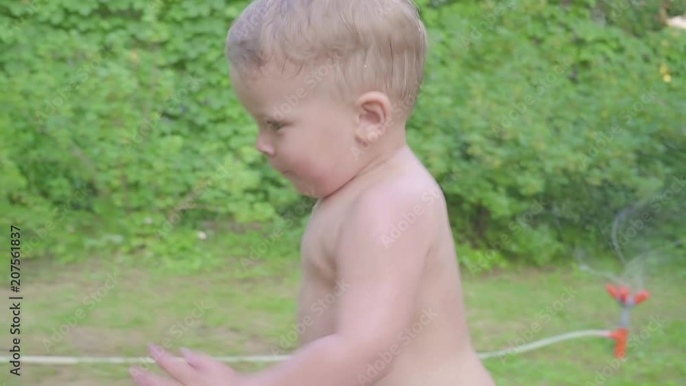 Cute little boy having fun outside with water sprinkler in summer garden. Slow motion Cute little boy having fun outside with water sprinkler in summer garden. Slow motion