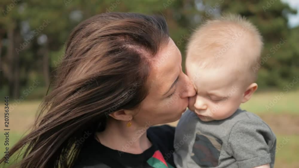 Happy family on nature outdoors mother kissing little baby boy on the green meadow. Happy family on nature outdoors mother kissing little baby boy on the green meadow.