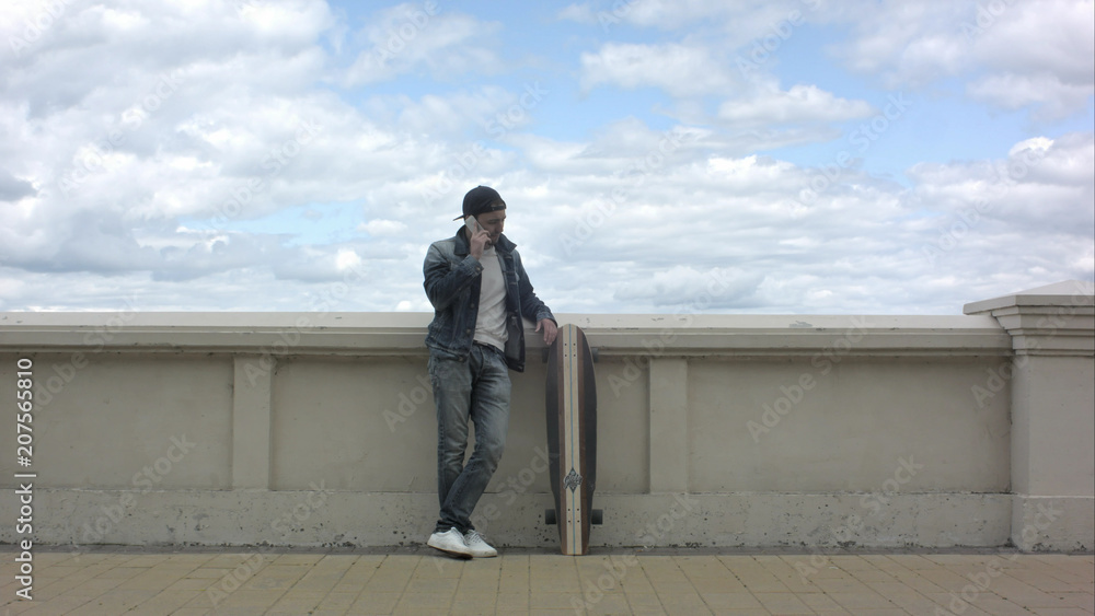 Smiley skateboarder standing outdoor and talking phone .