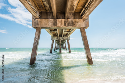 Under Okaloosa fishing pier in Fort Walton Beach, Florida during day with pillars, green shallow waves in Panhandle, Gulf of Mexico during sunny day photo