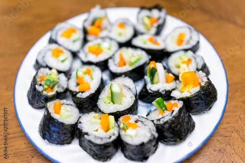 Closeup of handmade homemade maki California vegetable sushi pieces plain with white rice, orange bell pepper, marinated green cucumbers, avocado on plate
