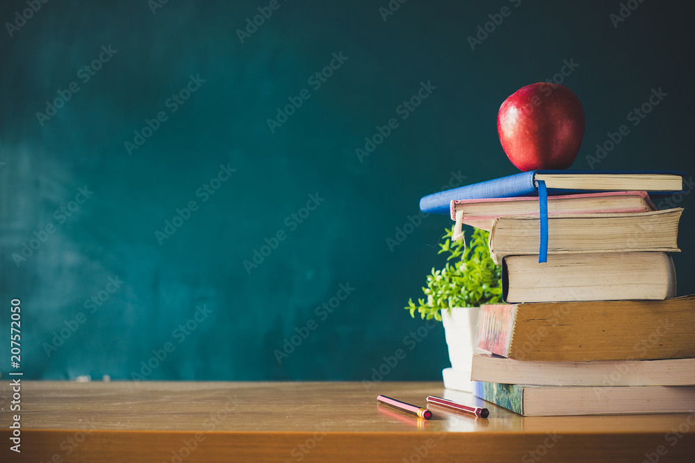 School books with red apple on desk over green school board background ...