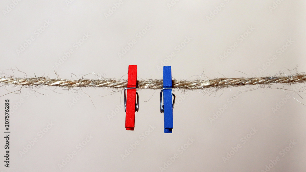A red clothespin and a blue clothespin hanging from a rope. A red clothespin and a blue clothespin hanging from a rope.