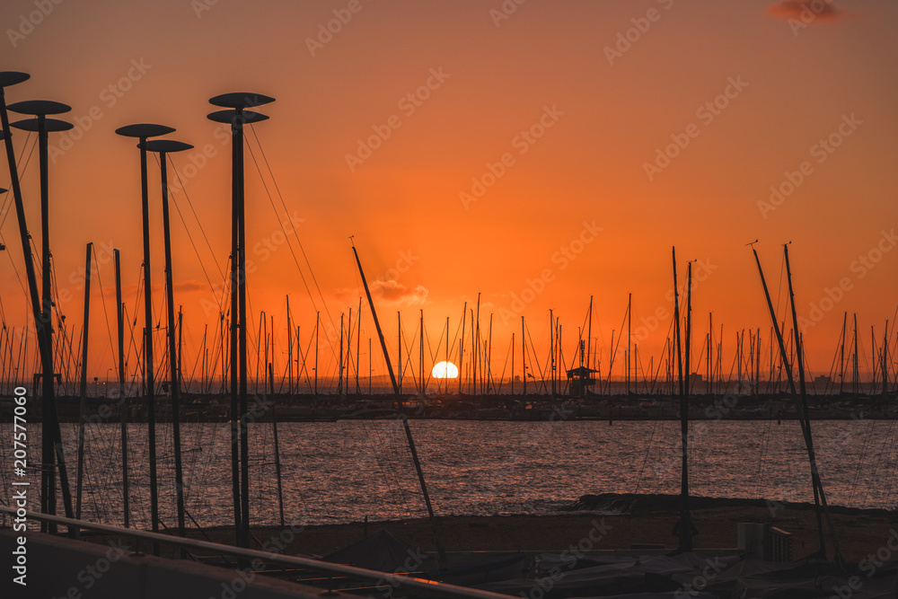 Sunset over water behind boats and yachts at marina
