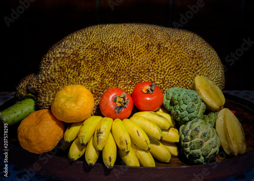 Tripical fruit arrangement in wooden bowl against black background photo