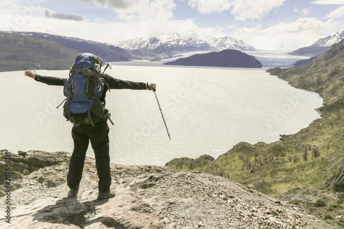 Homem de braços aberto com mochila em um mirante de pedrasolhando em direção a um glaciar.