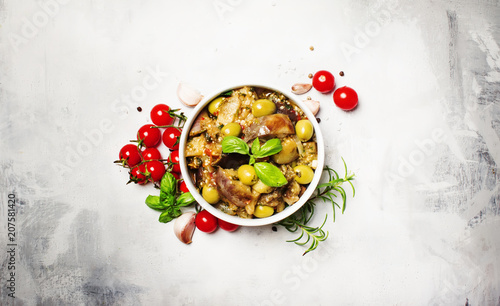 Stewed aubergines with vegetables and herbs in a bowl, light background, top view