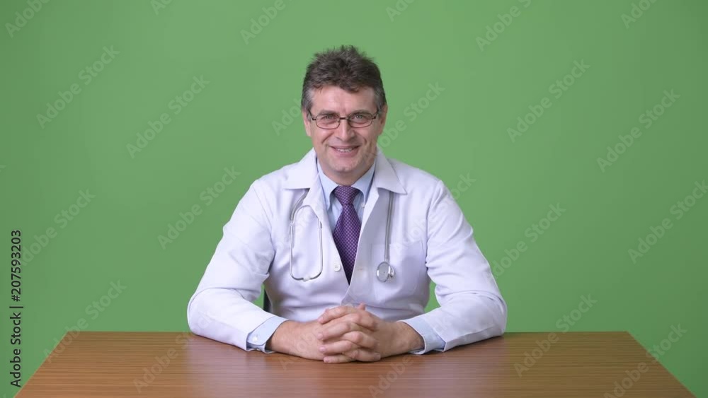 Mature handsome man doctor against green background