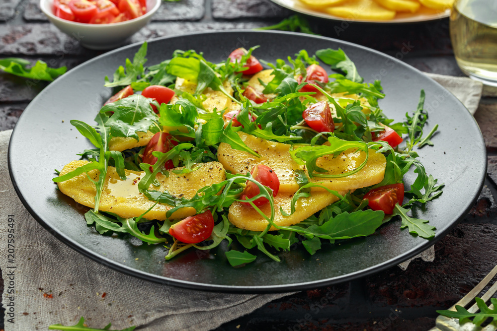 Polenta salad with sea salt, tomatoes, green rocket in a black plate. Polenta salad with sea salt, tomatoes, green rocket in a black plate.