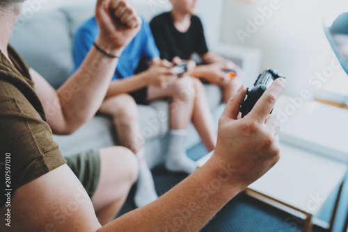 Father and sons sitting on a sofa in living room and playing video games. Family relaxing time at home concept.