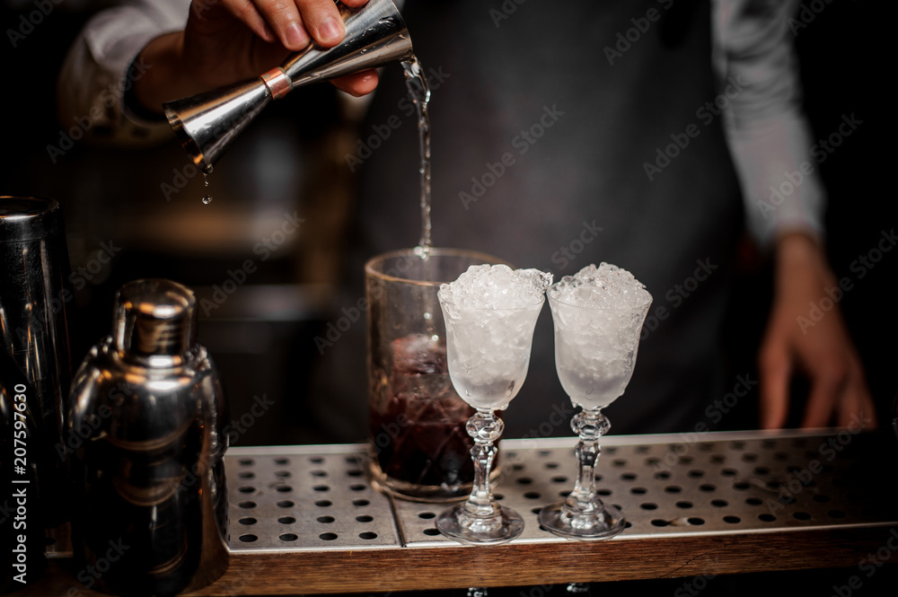 Bartender pouring alcoholic drink into the glass for making fresh summer cocktails