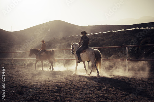 ride horses lessons at the sunset with golden backlight. dust and two horses and caucasian cowboy style people. vacation and leisure outdoor in feeling with the nature and the animals