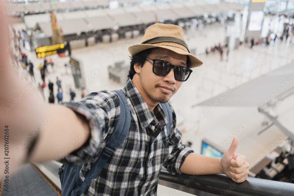 Asian man tourist taking a selfie with smart phone camera in airport.