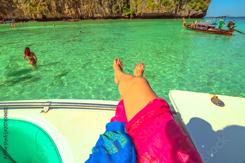 Woman's tanned legs on a tourist boat in the tropical and idyllic lagoon of the popular Maya Bay, Ko Phi Phi Leh in Phi Phi Islands, Krabi, Andaman Sea. Vacation, lifestyle and sunbathing concept.