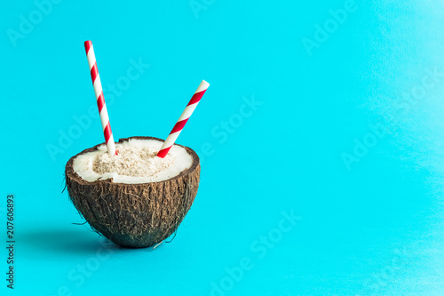 Coconut with drinking straws isolated on blue background. Space for copy.