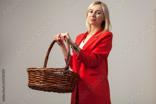 Young beautiful white blond girl in a bright red strict suit with a jacket and white blouse standing in a pose with empry Wicker basket on a white isolated background photo