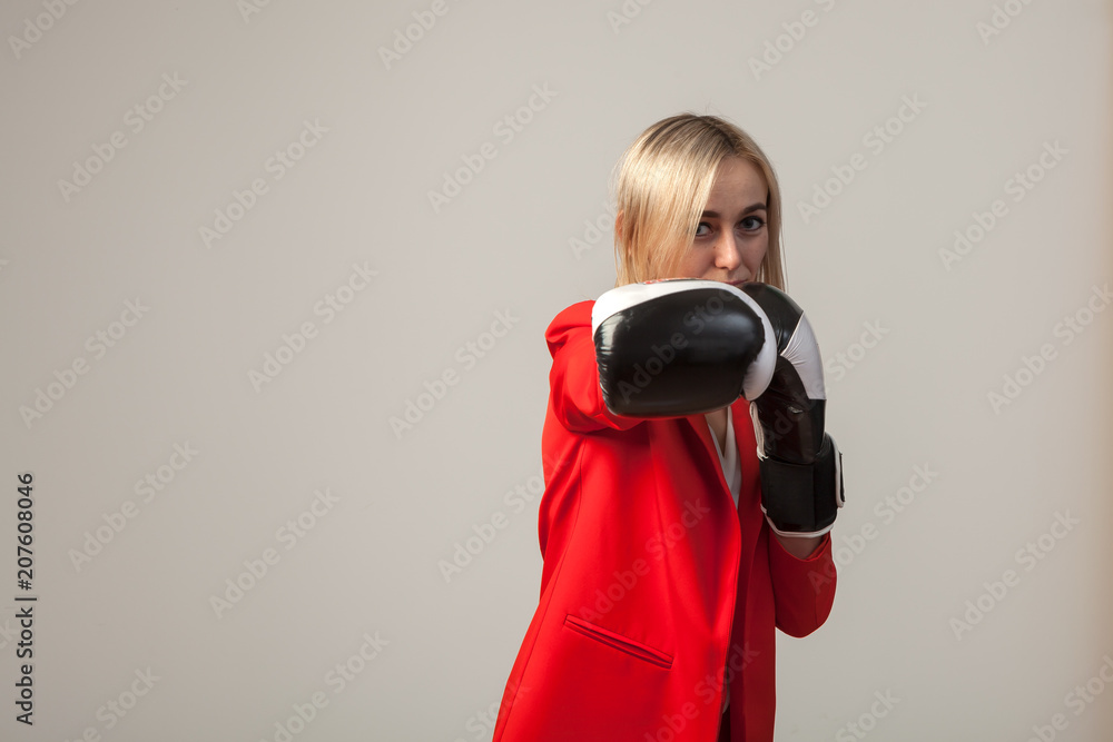 Obraz premium Young beautiful white blond girl in a bright red strict suit with a jacket and white blouse standing in a pose with boxing gloves on a white isolated background