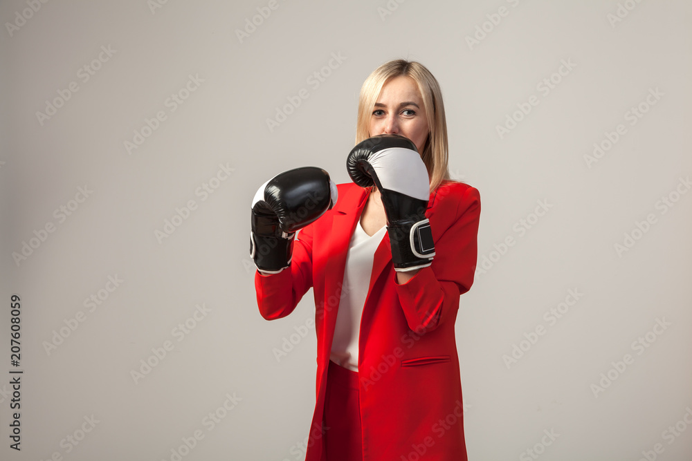 Obraz premium Young beautiful white blond girl in a bright red strict suit with a jacket and white blouse standing in a pose with boxing gloves on a white isolated background