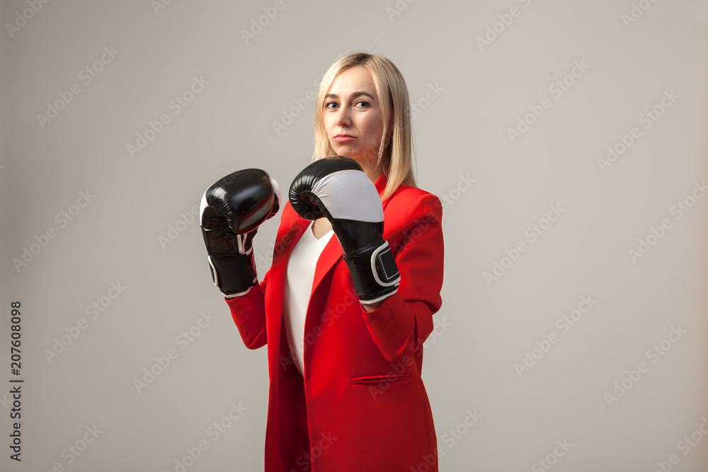 Young beautiful white blond girl in a bright red strict suit with a jacket and white blouse standing in a pose with boxing gloves on a white isolated background Young beautiful white blond girl in a bright red strict suit with a jacket and white blouse standing in a pose with boxing gloves on a white isolated background