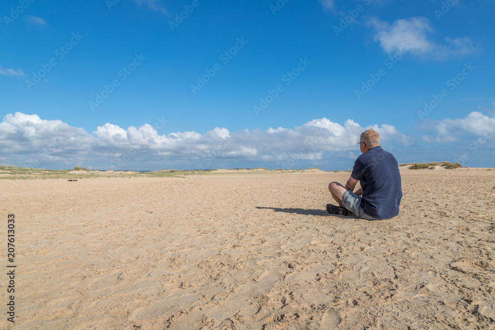 Im Sand sitzender Mann mit einem Blick in die Ferne