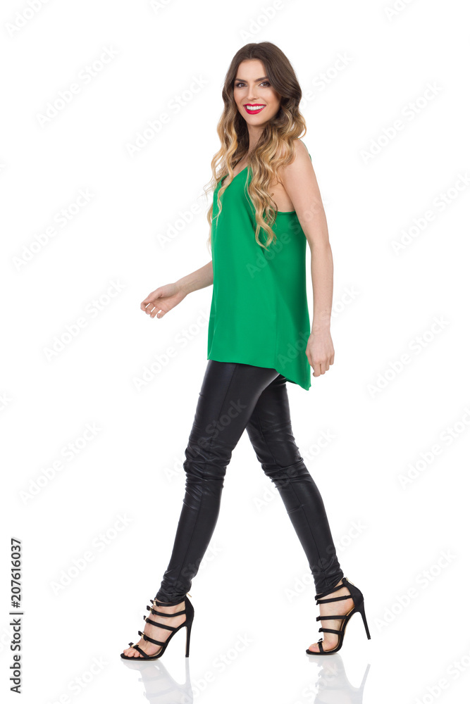 Walking Woman In Leather Trousers And High Heels Looking At Camera. Side View. Walking Woman In Leather Trousers And High Heels Looking At Camera. Side View.
