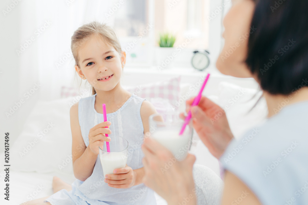 Pretty cute small child drinks delicious cocktail, has pleasant talk with her affectionate mother, enjoy together good morning, plan what to do during day off. Light tones. Spacious cozy bedroom Pretty cute small child drinks delicious cocktail, has pleasant talk with her affectionate mother, enjoy together good morning, plan what to do during day off. Light tones. Spacious cozy bedroom