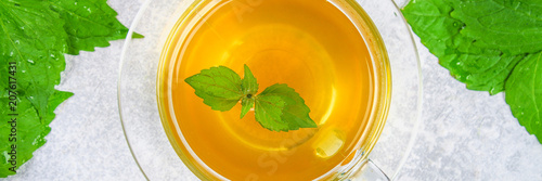 Leaves of fresh green nettle and a clear glass cup of herbal nettle tea on a gray concrete table. Top view.