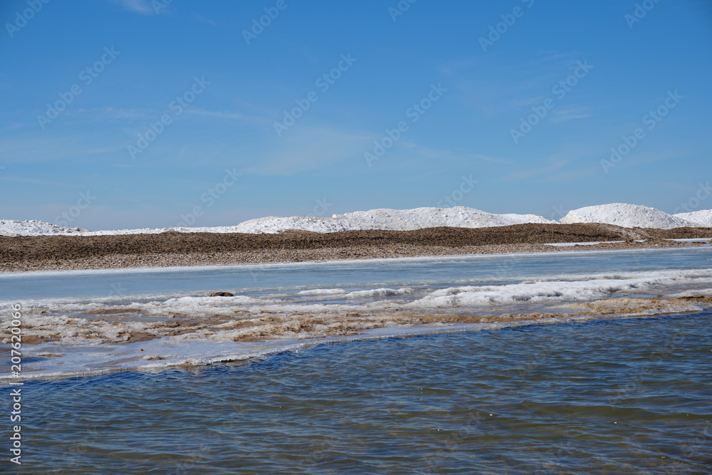Beautiful lake shore on spring day with ice and snow in water, blue sky in the background Beautiful lake shore on spring day with ice and snow in water, blue sky in the background