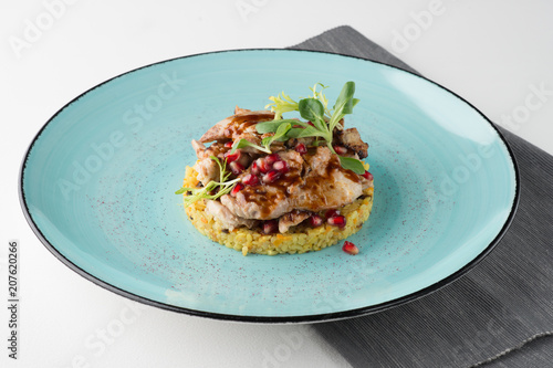 Meat with bulgur, pomegranate and fresh vendure on turquoise plate and napkin