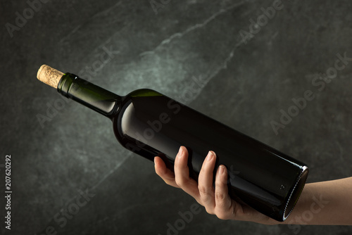 Hand is holding green wine bottle with cork on dark background