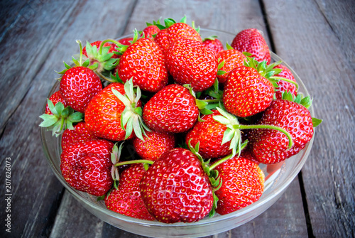 Juicy strawberries in a glass plate on a wooden background  