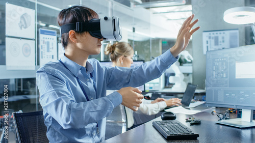 Computer Science Engineer wearing Virtual Reality Headset Works with 3D Modeling  Makes Gestures. In the Background Engineering Bureau with Busy Corowrkers.