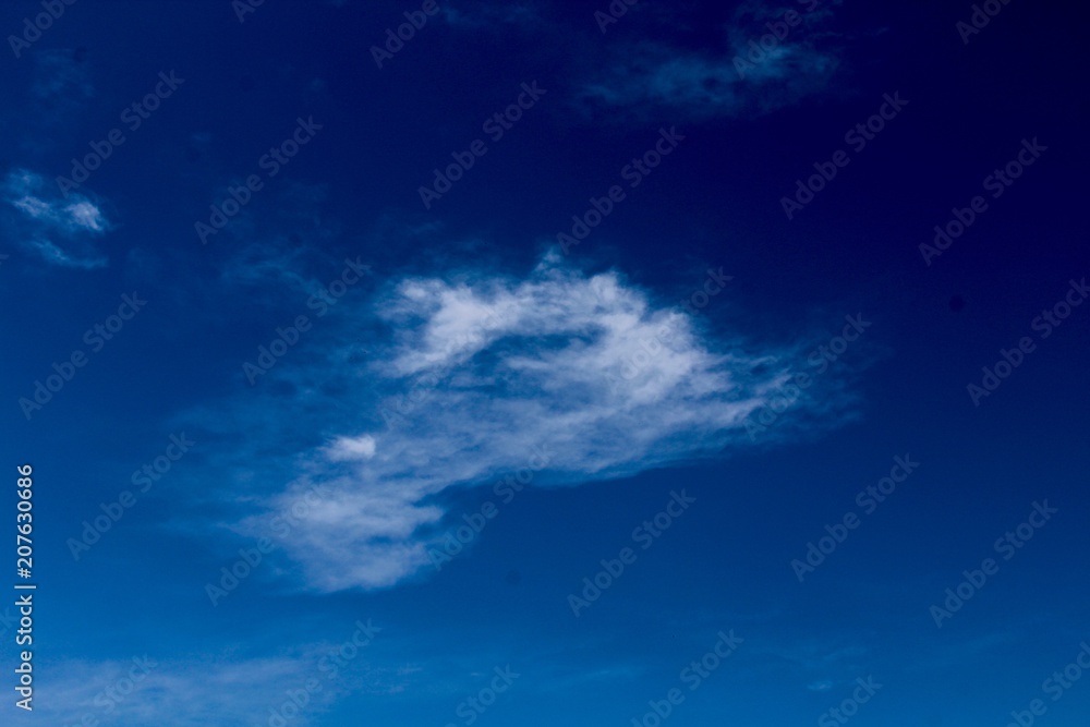 A small thin cloud in the bright blue sky in the air.
