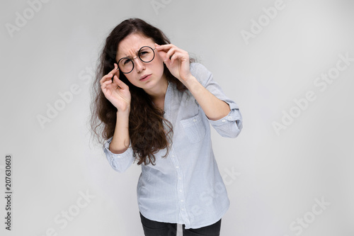 Portrait of a young girl in glasses. Beautiful young girl on a gray background. A young girl in a light blouse and dark trousers.