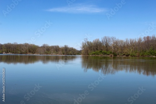 The trees reflection off the water of the river in the country.