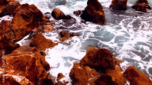 Swirling white sea water breaking on a rocky coastal shoreline viewed high angle with brown rocks photo