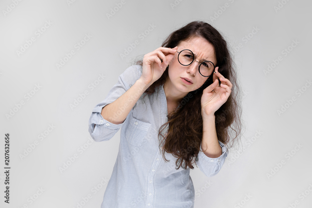 Portrait of a young girl in glasses. Beautiful young girl on a gray background. A young girl in a light blouse and dark trousers. Portrait of a young girl in glasses. Beautiful young girl on a gray background. A young girl in a light blouse and dark trousers.