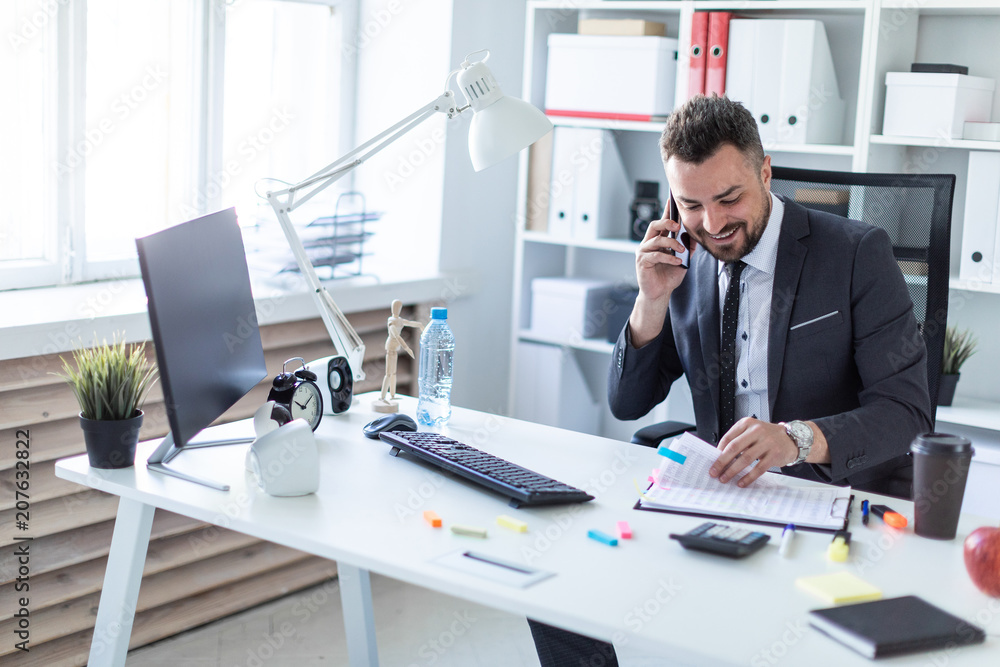 A man is sitting in the office at the table, talking on the phone and flipping through documents. A man is sitting in the office at the table, talking on the phone and flipping through documents.