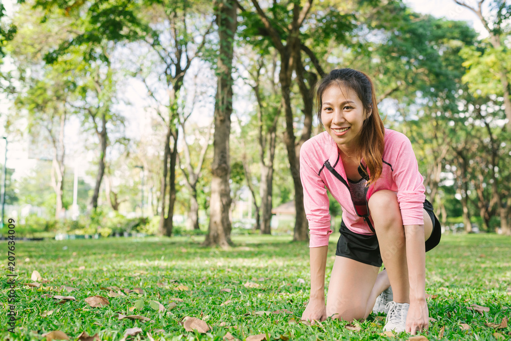 Asian young woman on mark to set ready for jogging exercise to buld up her body on glass in warm light morning. Young woman do exercise workout in park to make body beauty. Outdoor jogging in the park Asian young woman on mark to set ready for jogging exercise to buld up her body on glass in warm light morning. Young woman do exercise workout in park to make body beauty. Outdoor jogging in the park