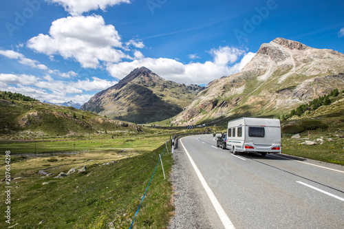 A caravan on the way to the vacations. Swiss mountains with a cloudy sky. Beautiful camping holidays with a camping car. Family travel in Europe. 
