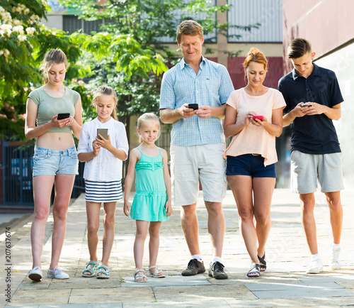 Portrait of happy large family standing with their mobile phones together outdoors