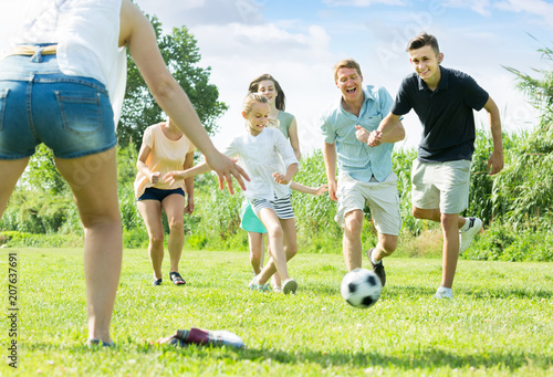 modern family of six people happily playing in football together outdoors
