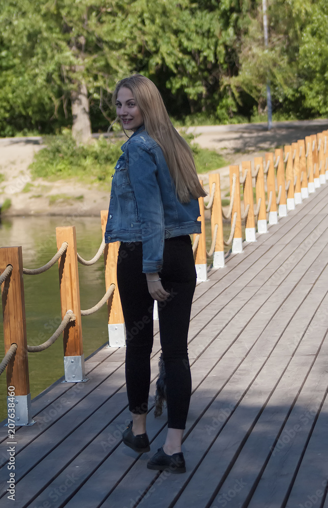 Beautiful blonde girl in denim jacket on nature background in full height. Girl looks back.