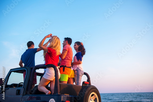 Young people having fun in convertible car at the beach at sunset.
