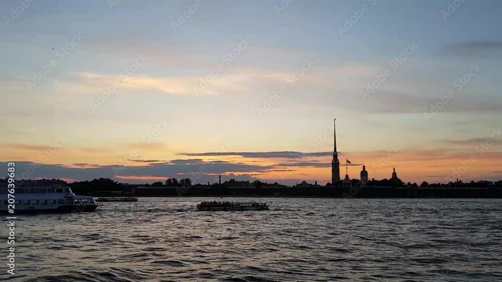 The Center Of St. Petersburg. On the river are sailing boats. In the sunset sun you can see the silhouette of the Peter and Paul fortress. Romantic frame. The ship turns on the water The Center Of St. Petersburg. On the river are sailing boats. In the sunset sun you can see the silhouette of the Peter and Paul fortress. Romantic frame. The ship turns on the water