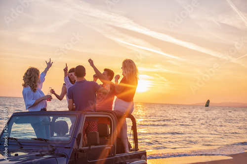 Young people having fun in convertible car at the beach at sunset.