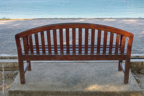 The brown wooden bench fixed on the concrete ground at the seaside.